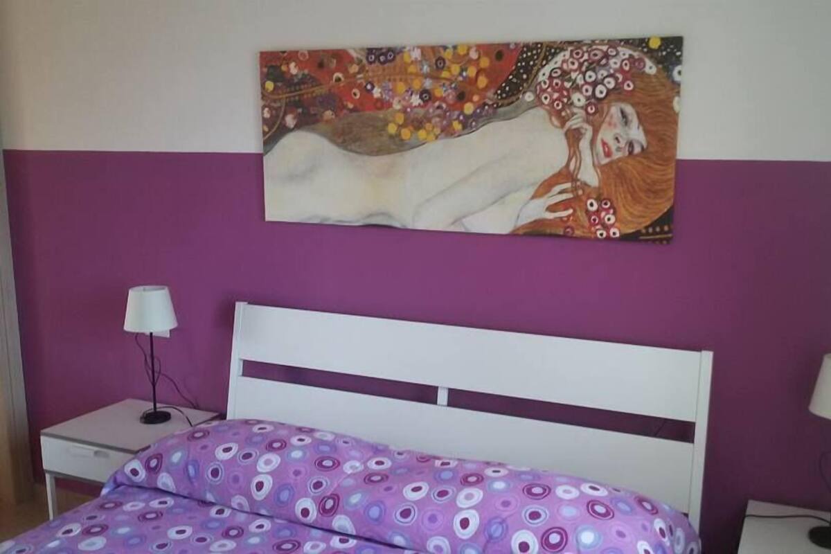Ein Schlafzimmer mit Bett, Nachttisch, Lampe und einem Bild an der Wand.
