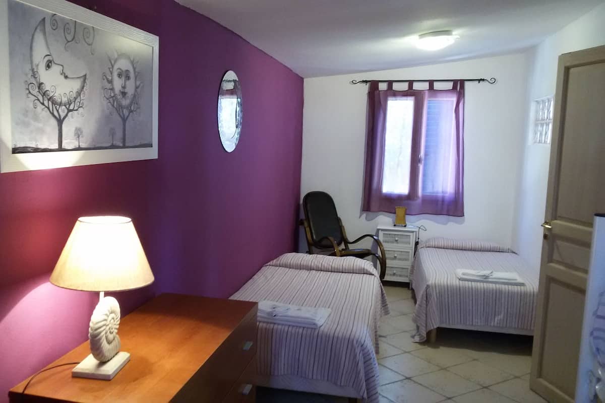 Ein Zimmer mit zwei Betten, einem Schreibtisch mit Lampe, einem Stuhl, einer Kommode und einem Fenster mit Vorhängen.