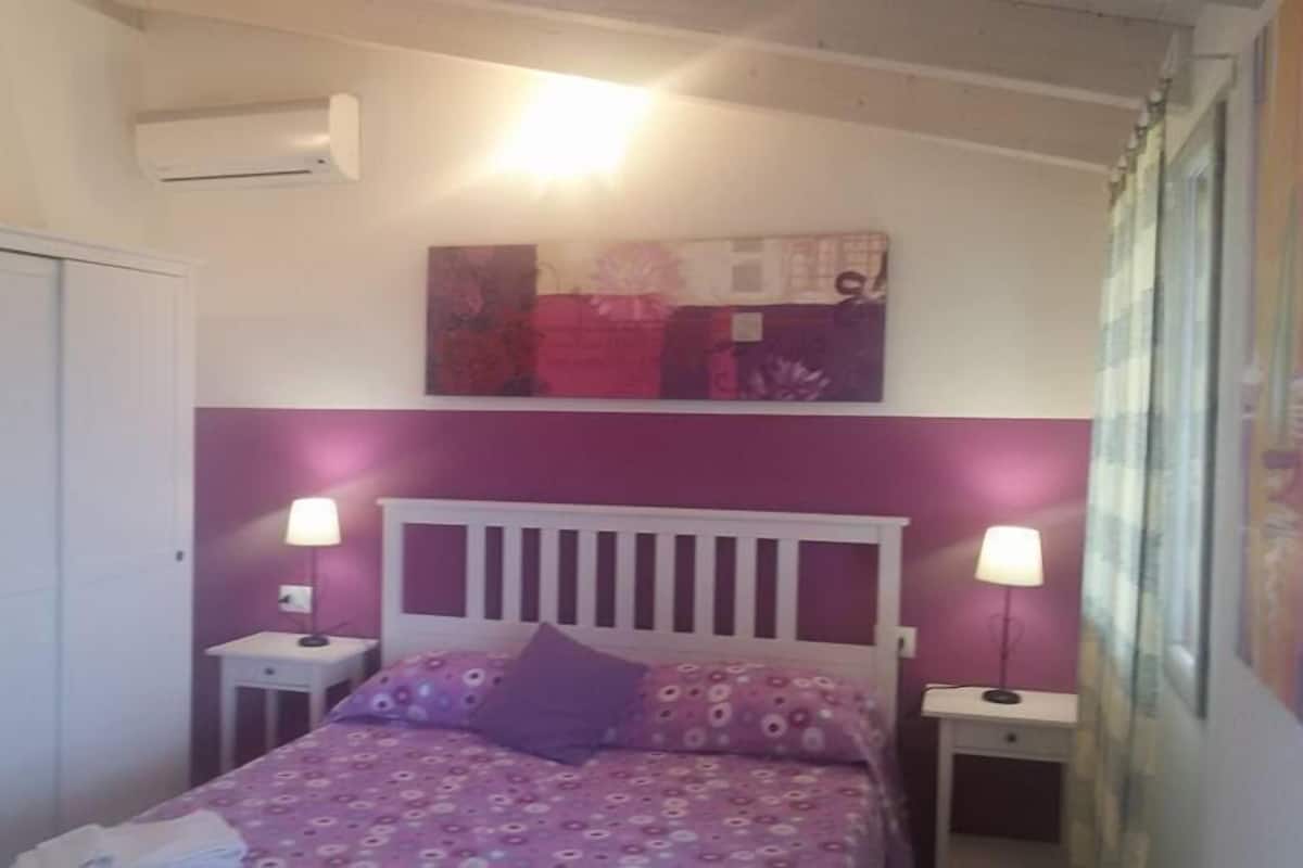Ein Schlafzimmer mit einem Bett, zwei Nachttischen, einem Kleiderschrank und einer Wand-Klimaanlage.