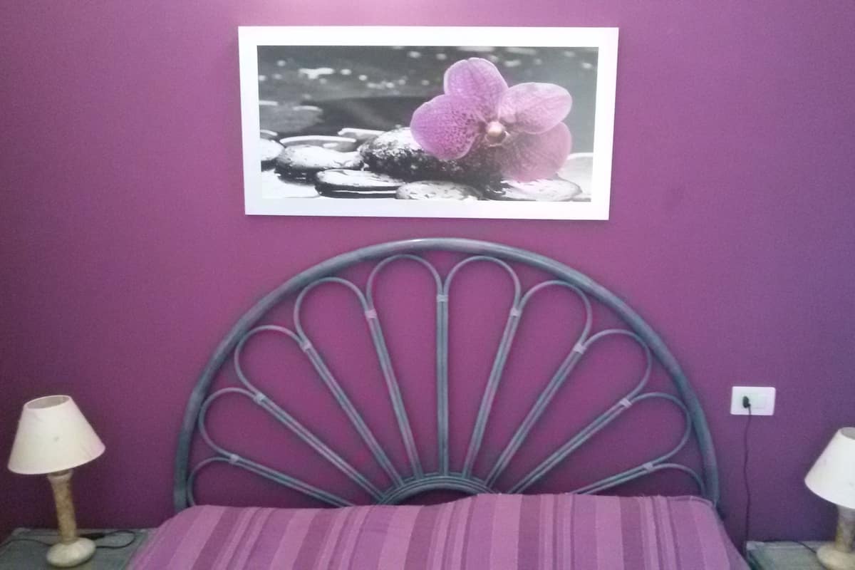 Ein Schlafzimmer mit violetter Wand, einem Bett mit Metallkopfteil und zwei Nachttischlampen.