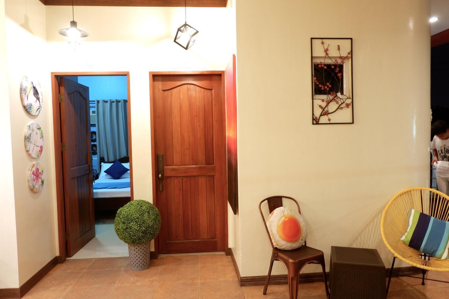A hallway with a wooden door, a small potted plant, a chair with a cushion, and a wall-mounted picture.