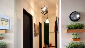 A hallway with a fire exit sign, a framed picture, a geometric pendant light, and wooden plant shelves.