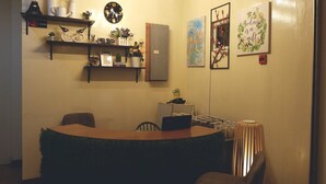 A cozy dining area with a round table, chairs, and a decorative plant. There are shelves with various items and a clock on the wall.