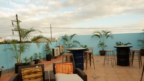 A rooftop patio with wicker furniture, potted plants, and a blue wall.