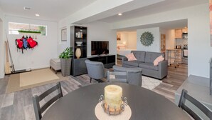 A modern living room with a dining table, grey sofas, a TV, and a kitchen in the background. - Relaxing Lakefront Suite (Federal Way)