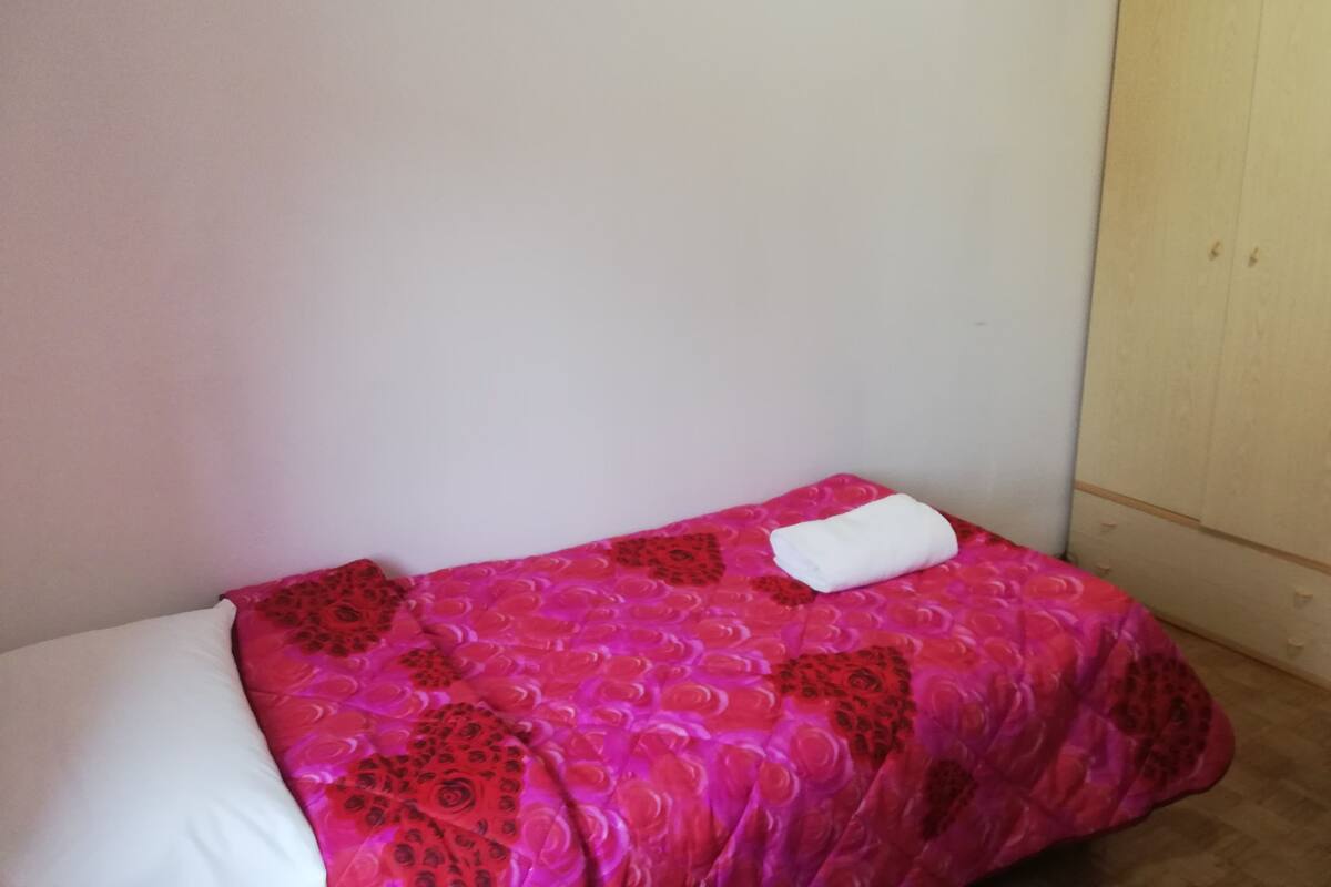 A small, single-bed room with a pink floral bedspread and a white pillow.