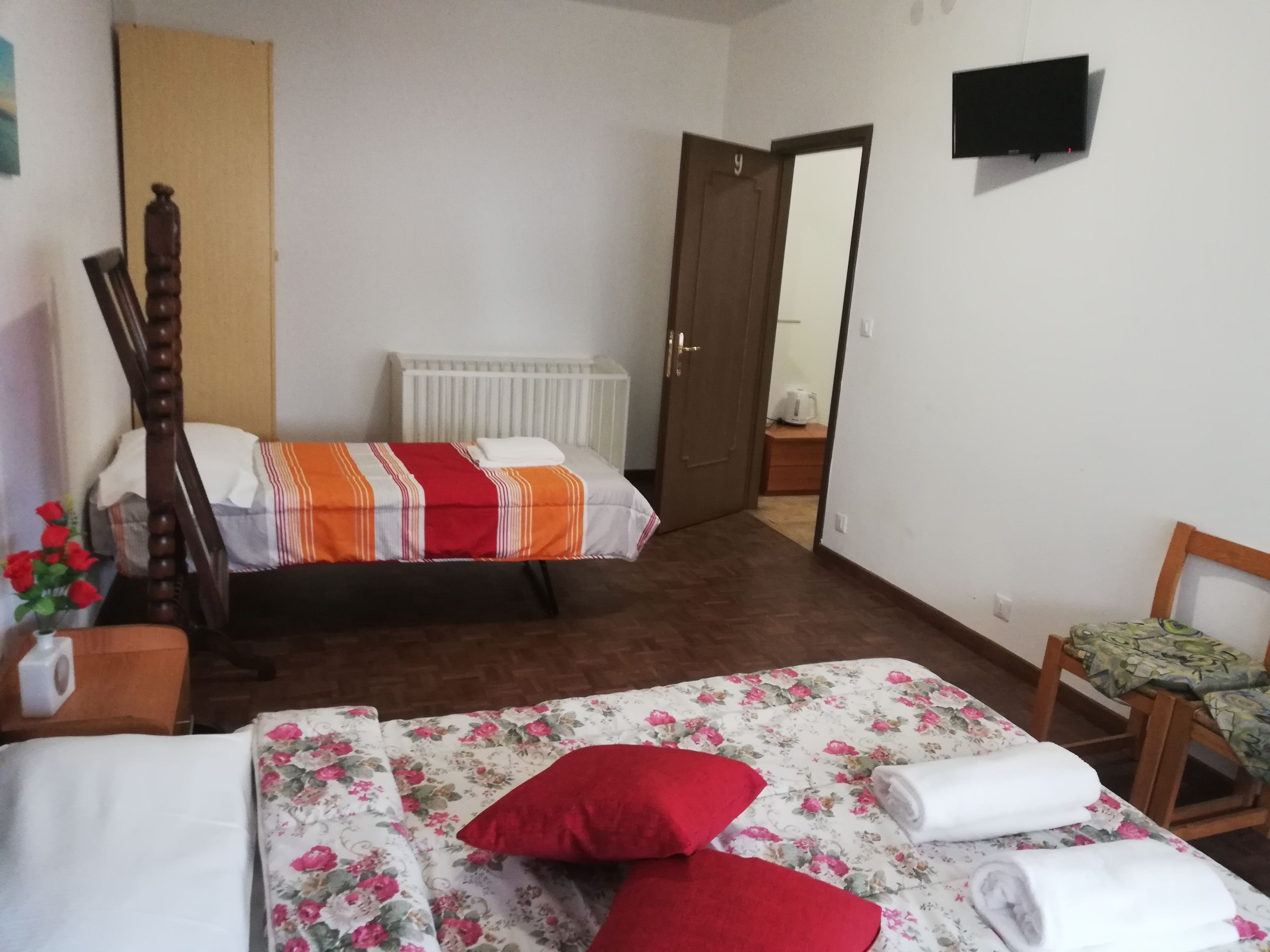 A bedroom with two beds, a wooden chair, a radiator, and a television on the wall.