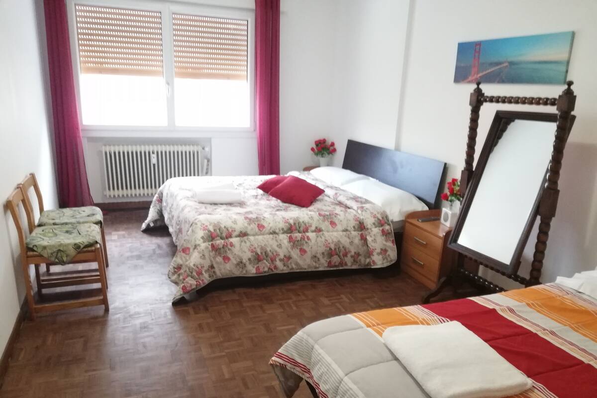 A bedroom with a bed, a chair, a dresser, a mirror, and a window with curtains.