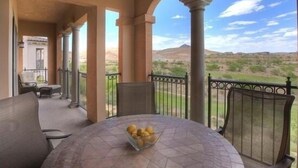 Eine überdachte Terrasse mit einem runden Tisch und Stühlen, einer Obstschale und Blick auf eine gebirgige Landschaft.