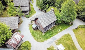 Un chalet rustique en rondins de bois, doté d’un toit de chaume, entouré d’une végétation luxuriante et bordé d’un chemin de gravier.