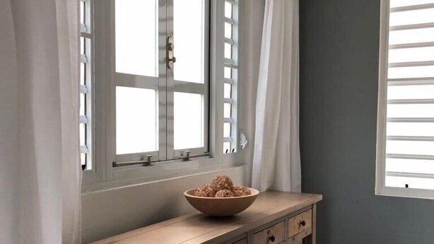 A kitchen with a wooden countertop, two windows with white curtains, and a bowl of noodles on the counter. - La Casita de Abuela (Hato Rey Central)