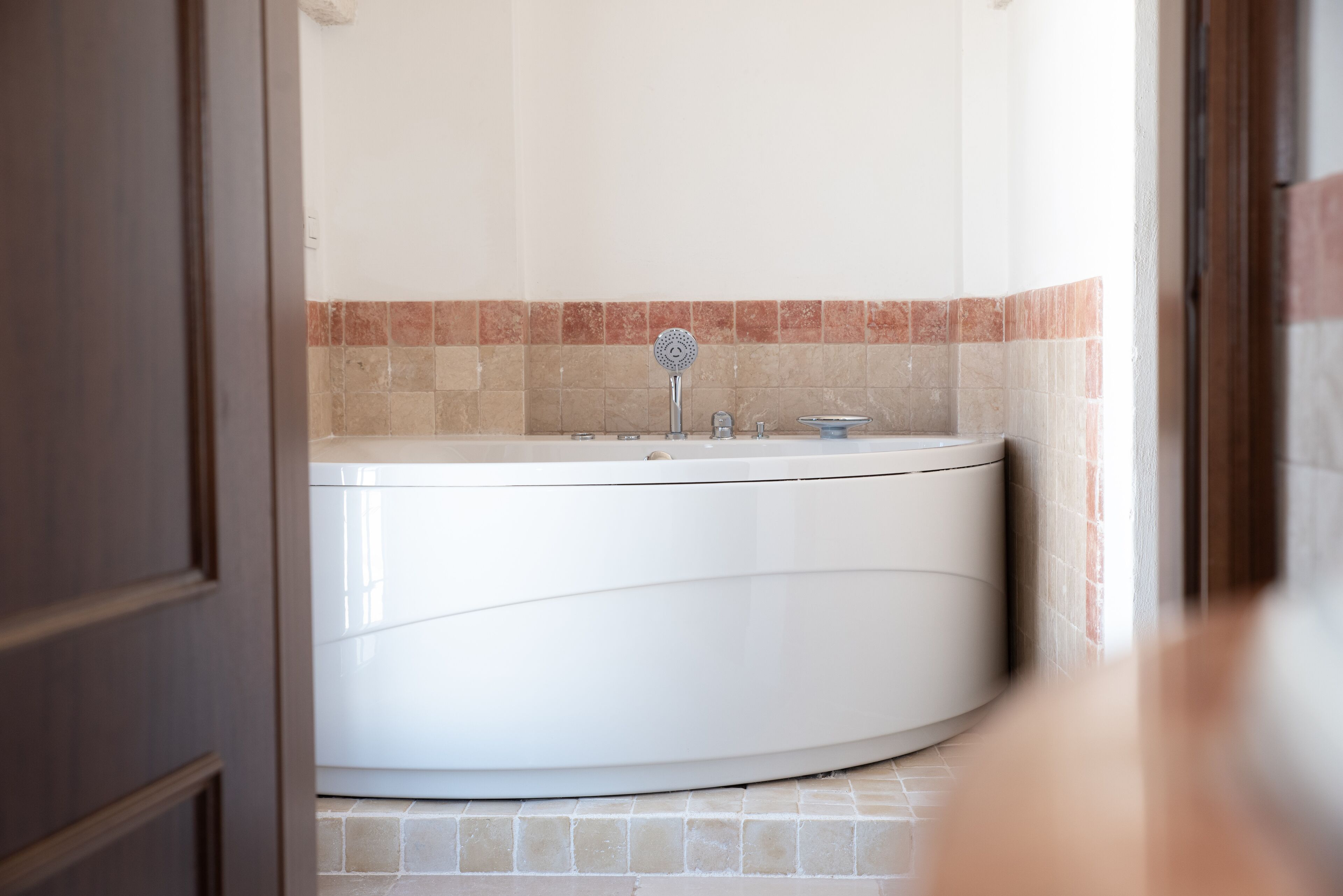 Un baño con una bañera blanca, un cabezal de ducha y una pared con azulejos.