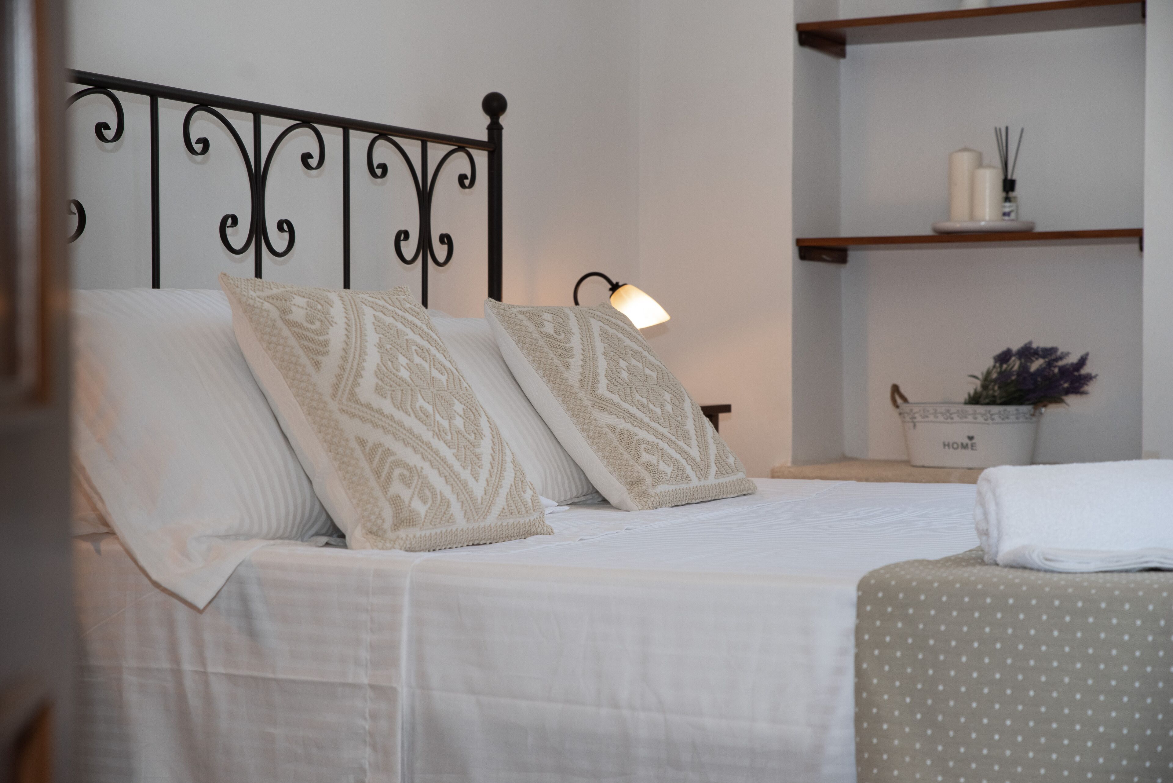 A neatly made bed with patterned pillows, a bedside lamp, and a shelf with decorative items.
