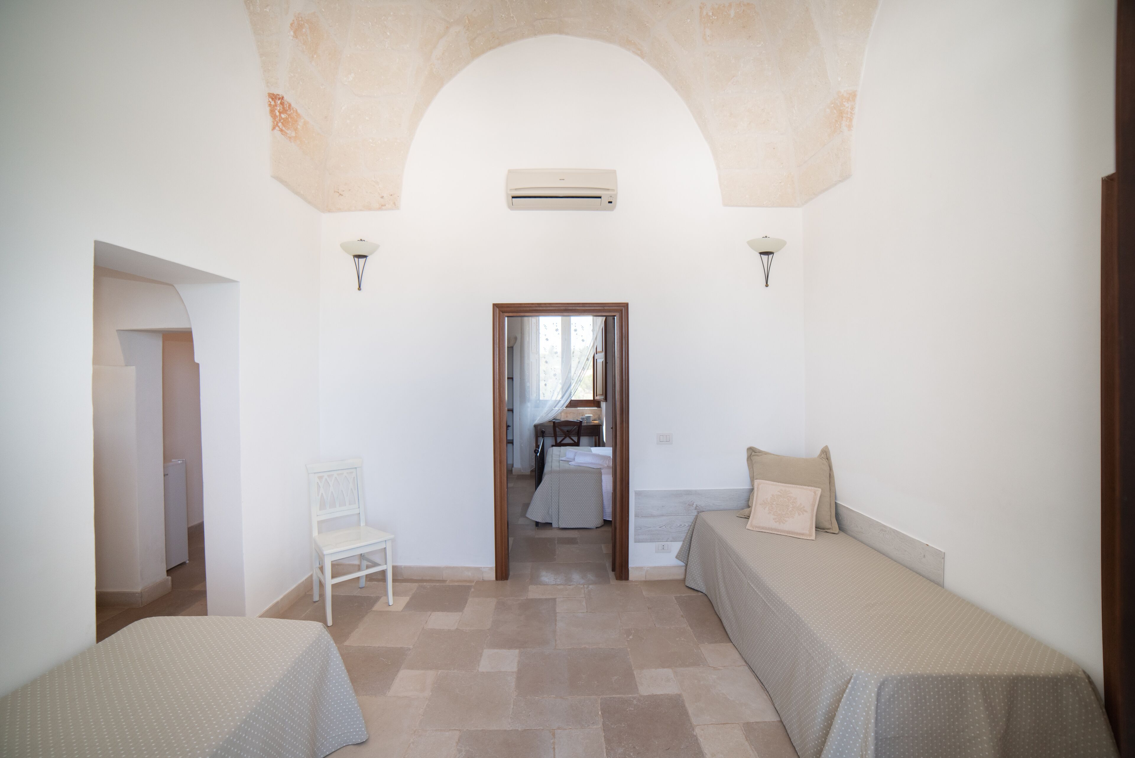 A bedroom with two beds, a chair, and a door leading to a bathroom.
