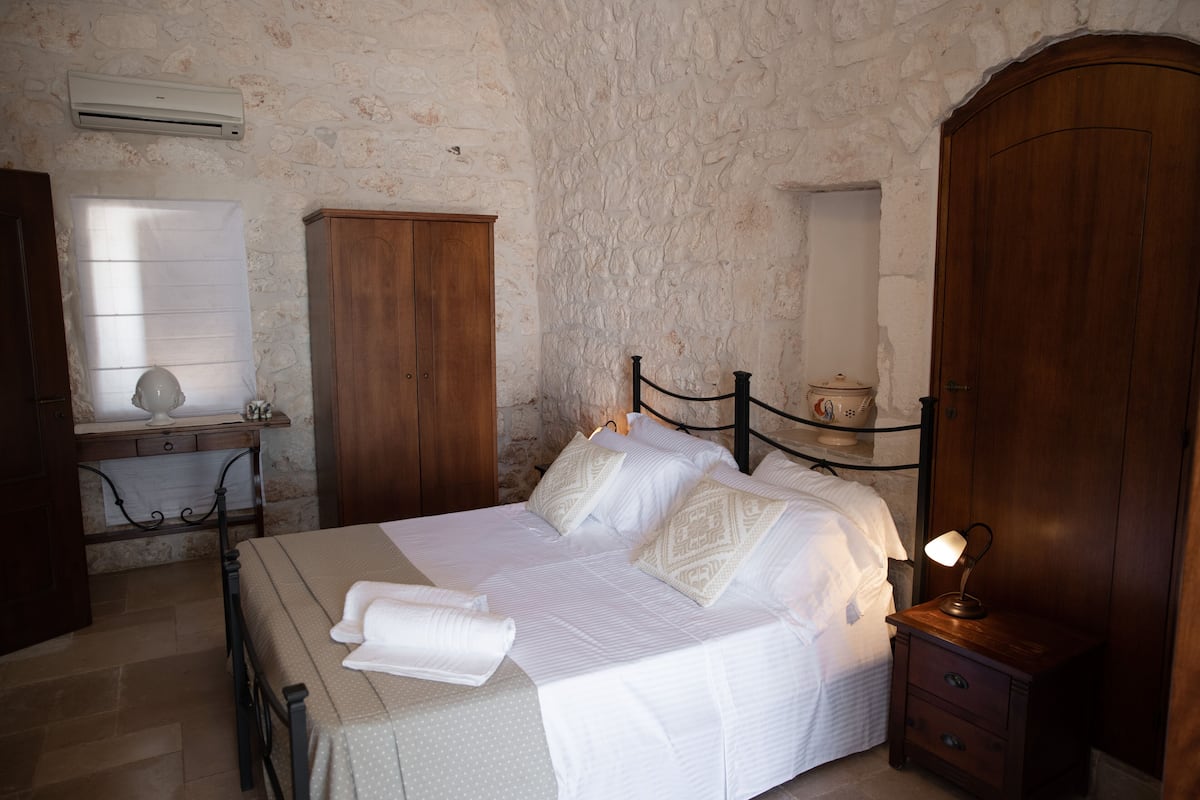 A bedroom with a bed, wooden wardrobe, bedside table, and an air conditioning unit.
