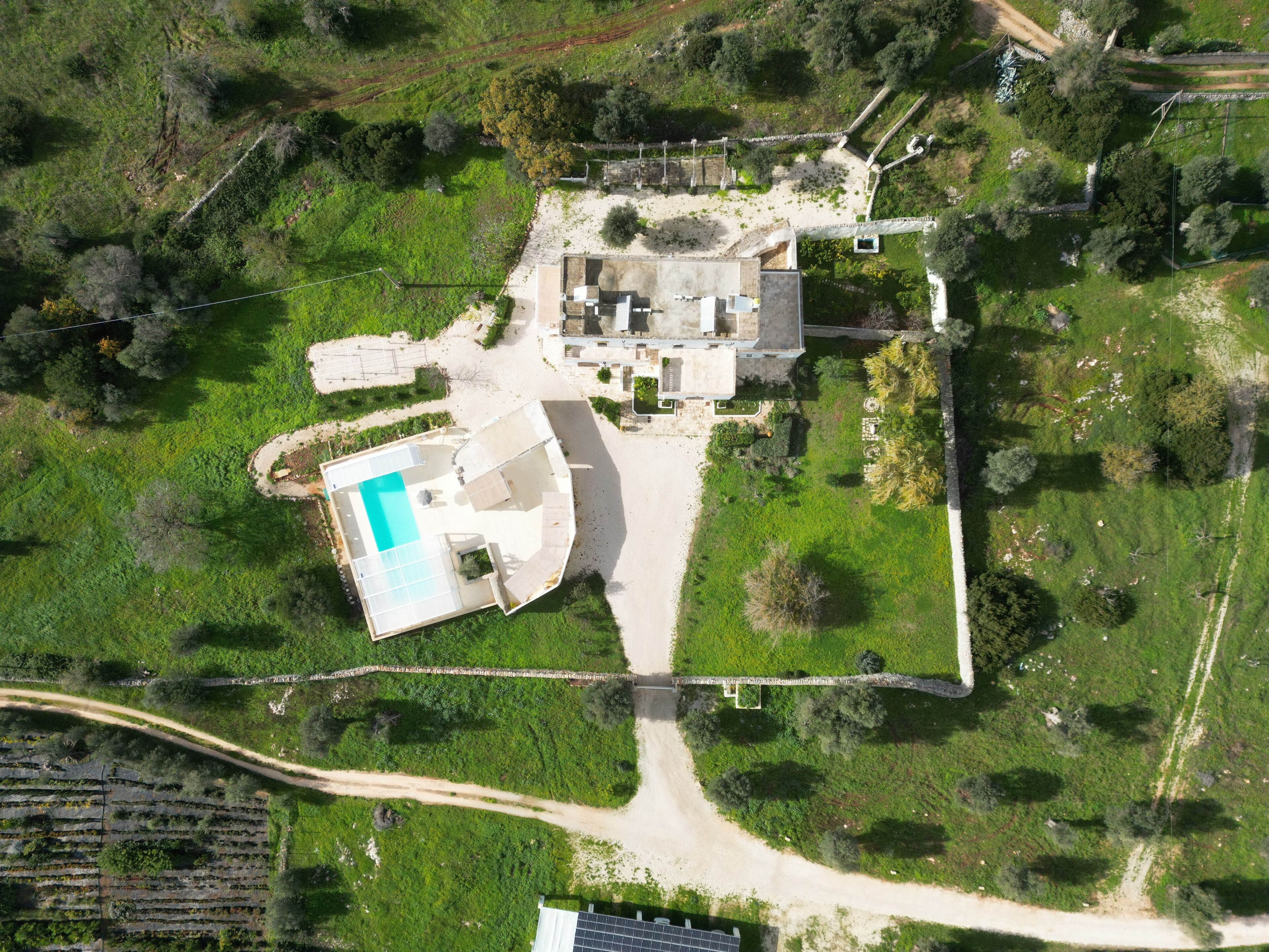 An aerial view of a property with a swimming pool, a large house, and surrounding greenery.