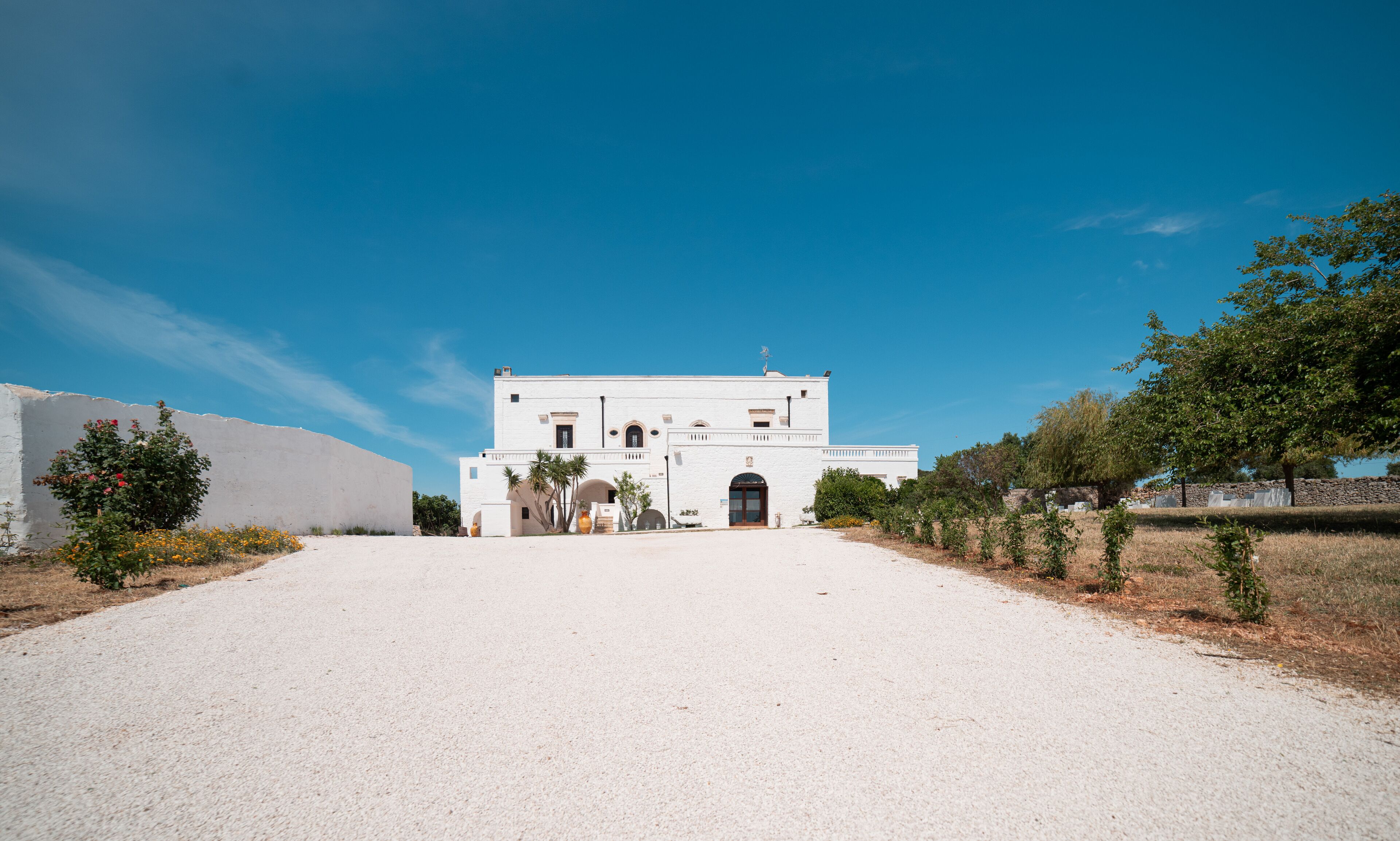 A white building with a central entrance, surrounded by a gravel path and sparse vegetation.