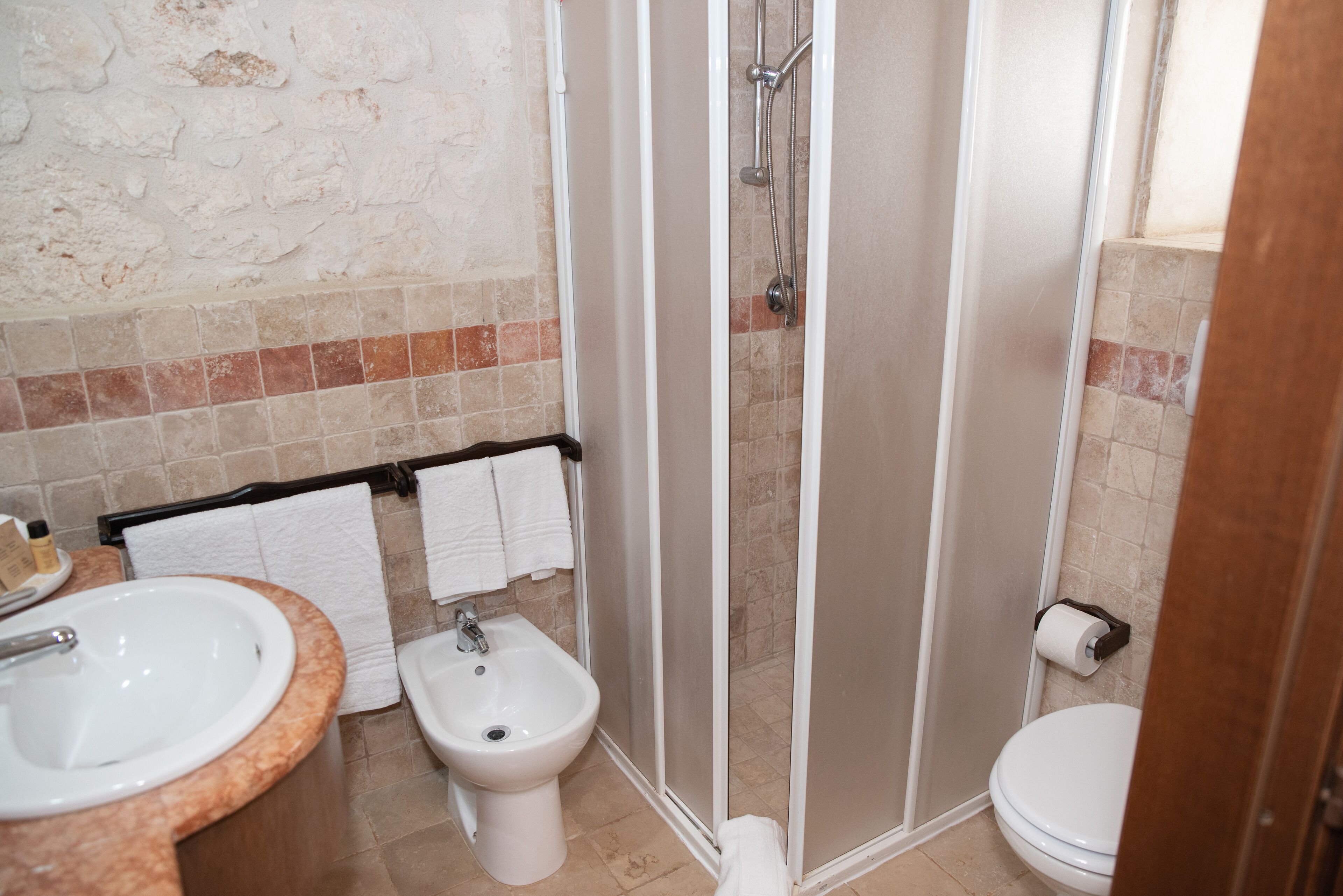 A bathroom with a sink, bidet, toilet, and a glass shower enclosure.