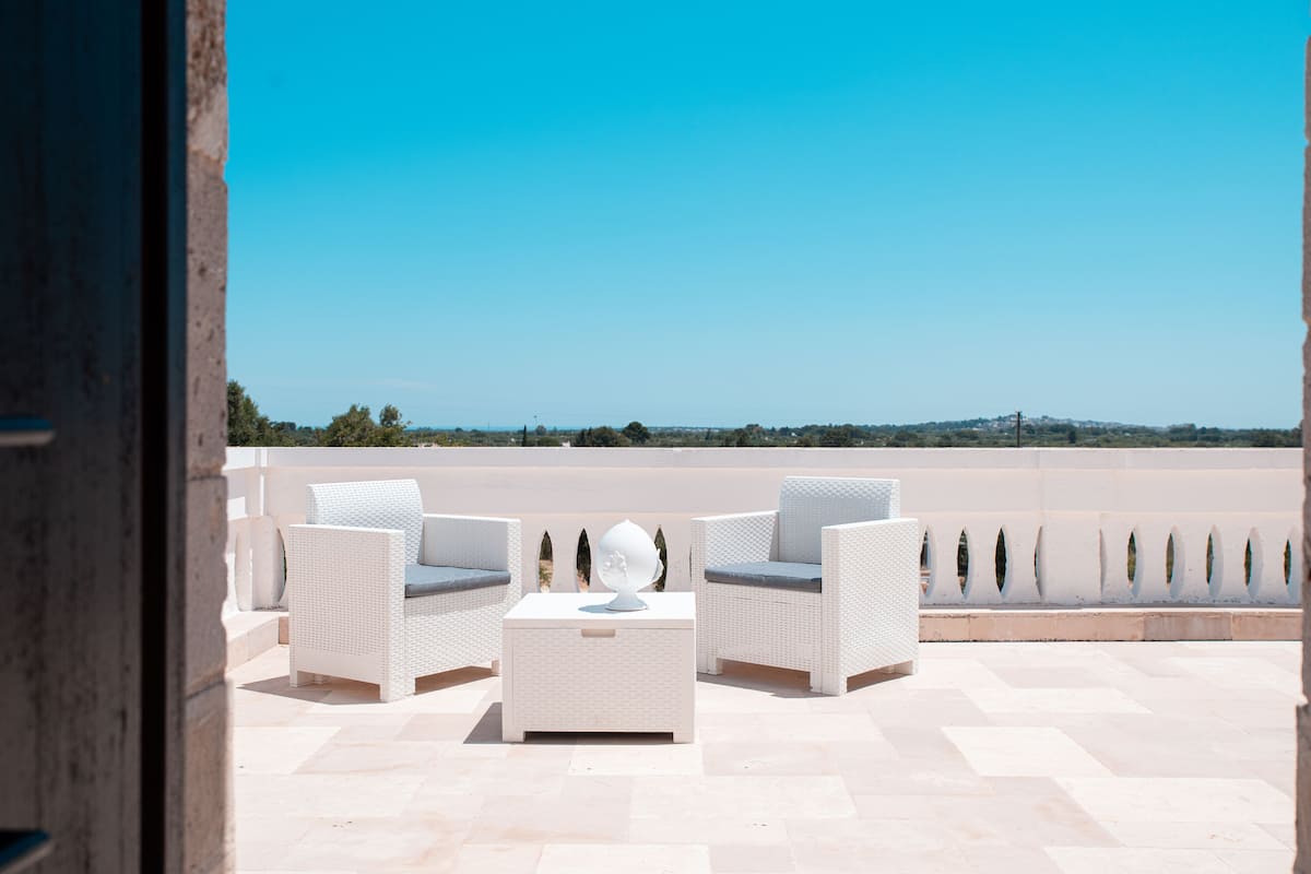 A terrace with white wicker furniture and a clear view of the landscape.