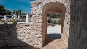 Une ancienne construction en pierre, dotée d’un portail en arc de cercle, entourée de murs de pierre et d’une clôture blanche.