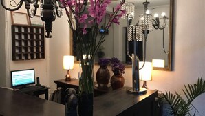 Una habitación bien iluminada con una computadora en un escritorio, un jarrón con flores y un espejo que refleja una lámpara de araña.