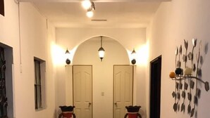 Un pasillo con piso a cuadros, un sofá rojo, una mesa con un florero y dos puertas al final.