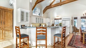 A spacious kitchen with wooden beams, white cabinets, and a central island with bar stools.