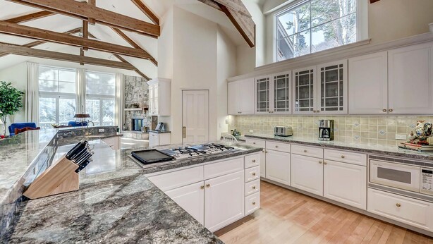 A spacious kitchen with white cabinets, a granite countertop, and a large window.