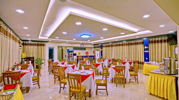Un grand espace dédié à la salle à manger, avec plusieurs tables et chaises, une horloge au mur et une porte bleue en arrière-plan.