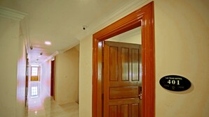 Un couloir d’hôtel avec un sol ciré et une porte en bois. Une pancarte sur le mur indique le numéro de la chambre : 401.