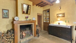 Ein gemütliches Zimmer mit Kamin, Holzbalken, einer Kommode mit Schubladen und einem Spiegel an der Wand.