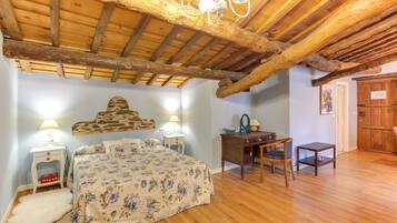 Un dormitorio con techo de madera, una cama con ropa de cama floral, un escritorio y una silla.