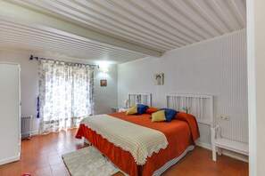 Une chambre à coucher avec un lit, une table de chevet, une chaise, un radiateur et une fenêtre avec des rideaux.