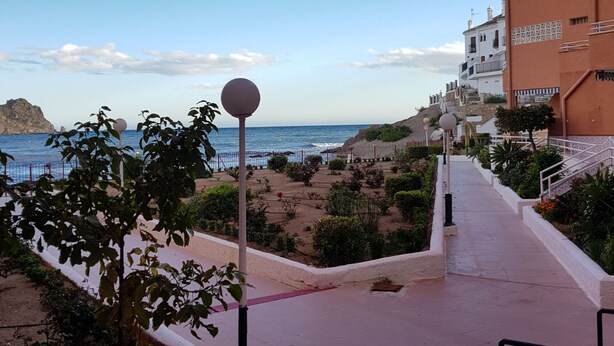 A coastal walkway with a view of the sea, a rocky outcrop, and a building with a white facade. - Miramar Habitaciones (Aguilas)