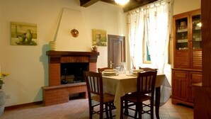 Un comedor con chimenea de ladrillo, sillas de madera, una mesa dispuesta para dos personas y un aparador con puertas de vidrio.