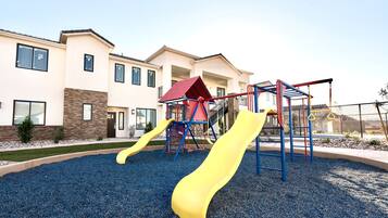 A playground with slides and climbing structures, surrounded by a building with multiple windows and a brick facade.
