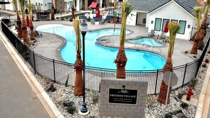 A swimming pool with palm trees, a sign for Freedom Village Vacation Rentals, and a building in the background. - ❀Aloha❀ - Tropical Island Retreat | POOL IS OPEN!!! Great Family Friendly Vacation! (Washington)