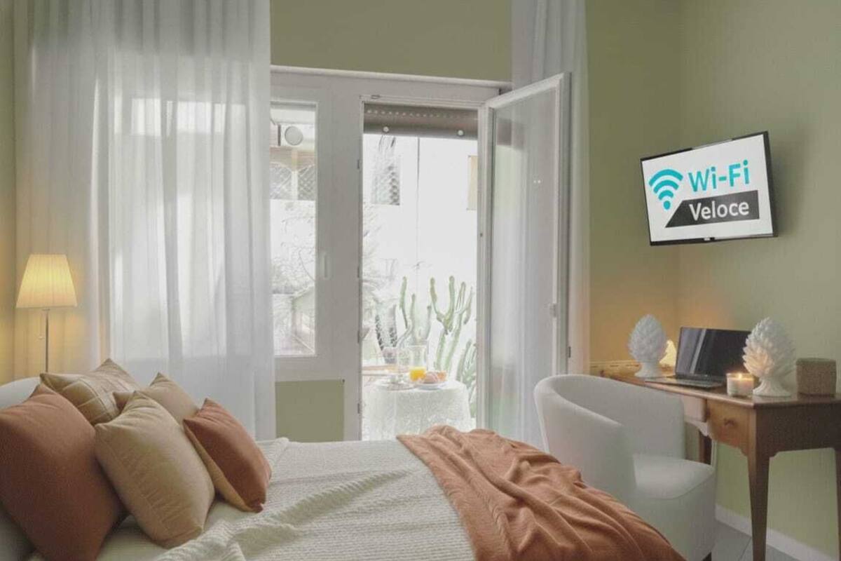 Une chambre d’hôtel équipée d’un lit, d’un bureau, d’une chaise, d’un téléviseur affichant les informations sur le service Wi-Fi, et offrant une vue sur des cactus à l’extérieur.
