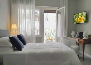 A hotel room with a bed, a desk with a computer, a TV, and a view of a cactus outside. - B&B 120 Rodionoff - connection to Airport and Mondello Beach (Palermo)
