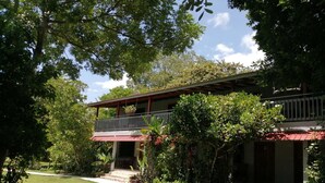 Una casa de dos pisos con balcón, rodeada de exuberante follaje y un césped cuidado.