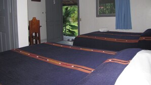 Una habitación con dos camas, una puerta que da al exterior, una ventana con cortina azul y una silla.