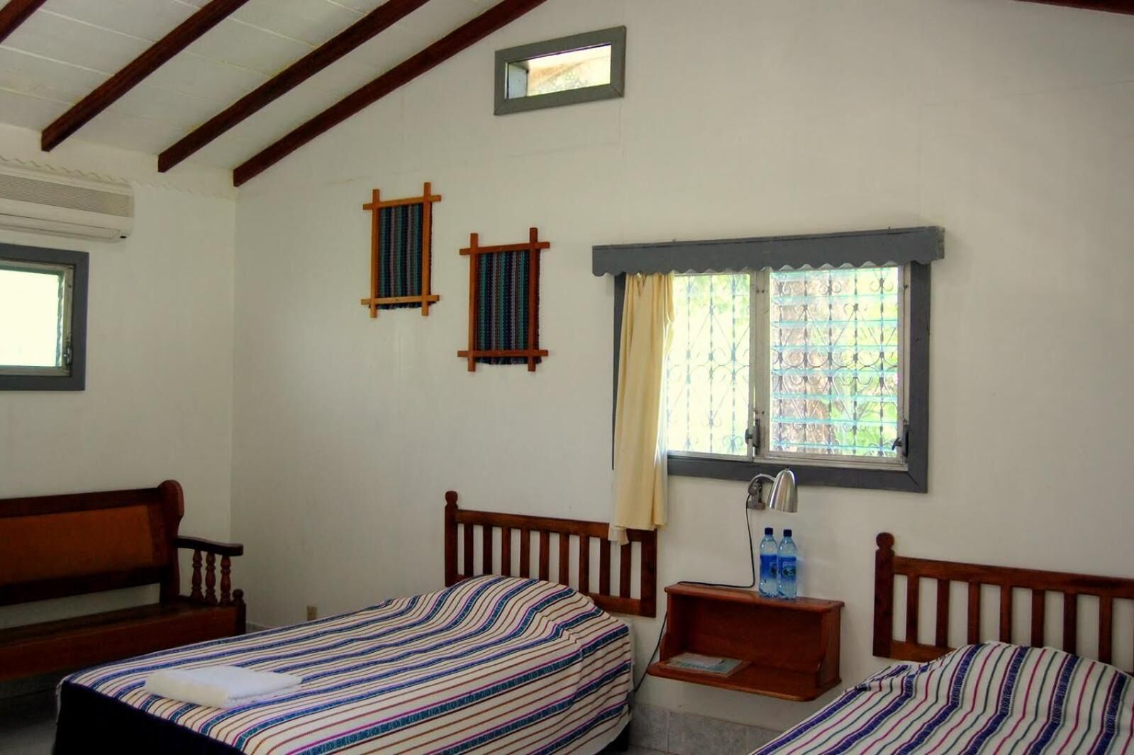 Une chambre avec deux lits, une petite table avec une lampe et une fenêtre avec un rideau.