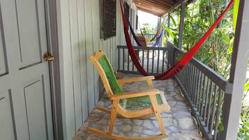 Een houten schommelstoel met een groene netrug op een terras met stenen tegels.