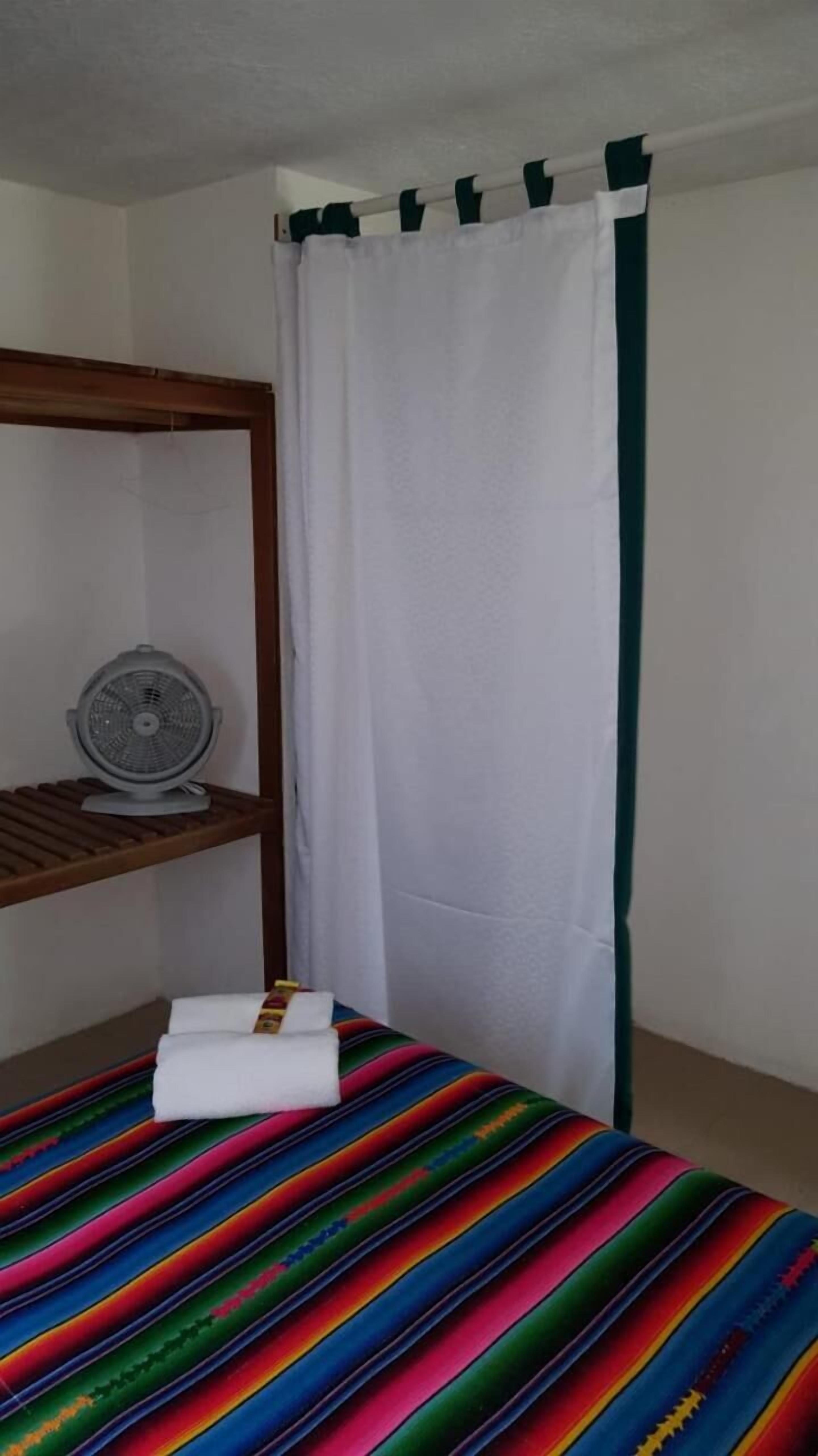 A room with a bunk bed, a small fan on a shelf, and a colorful bedspread.