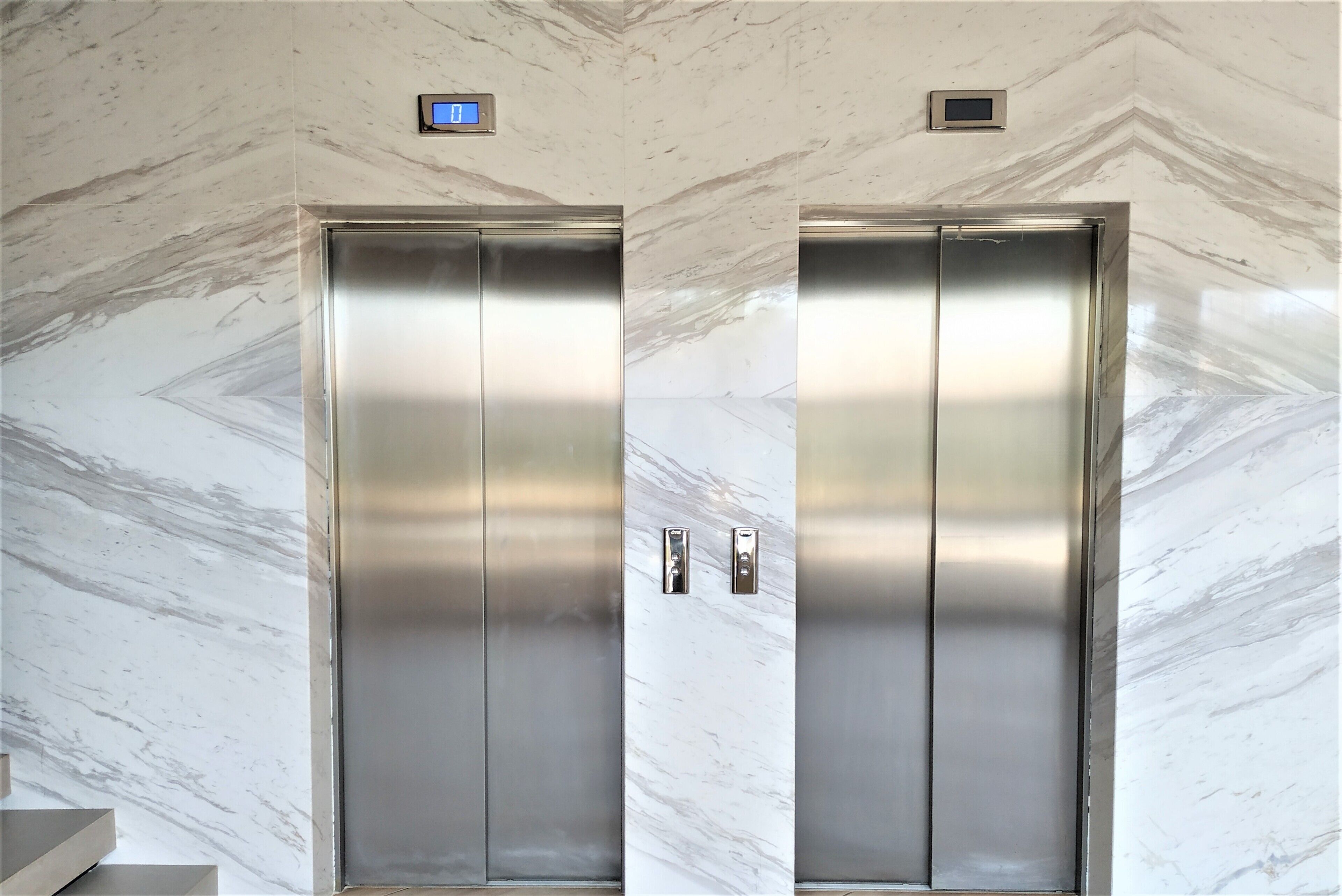 Two elevator doors with a marble wall background and a digital display above them.