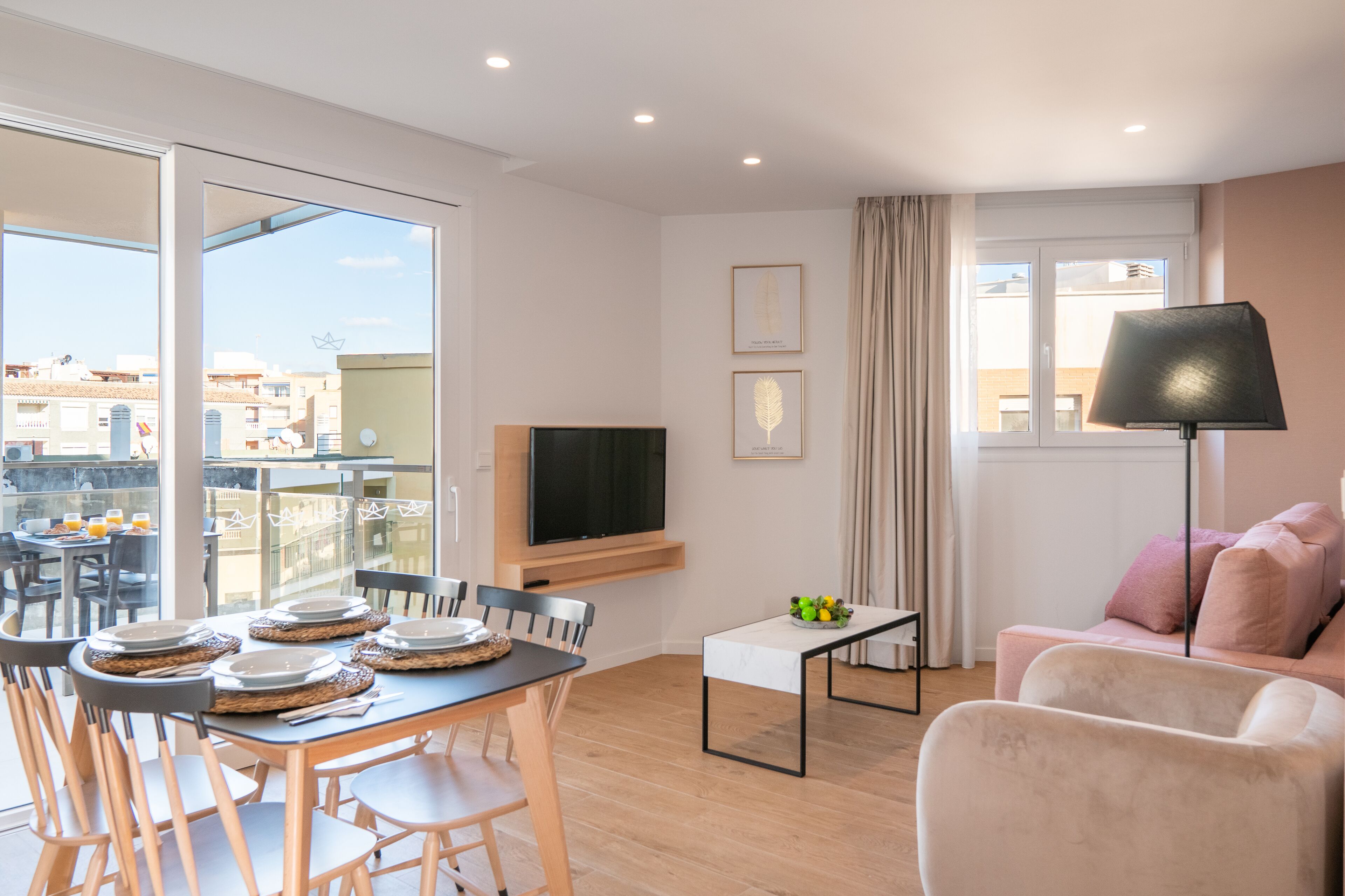 Ein modernes Wohnzimmer mit Essbereich, einem Flachbildfernseher und einem Balkon mit Blick auf Gebäude.