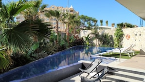 A swimming pool with lounge chairs, surrounded by tropical plants and a stone wall. - Ahoy Apartments (El Campello)