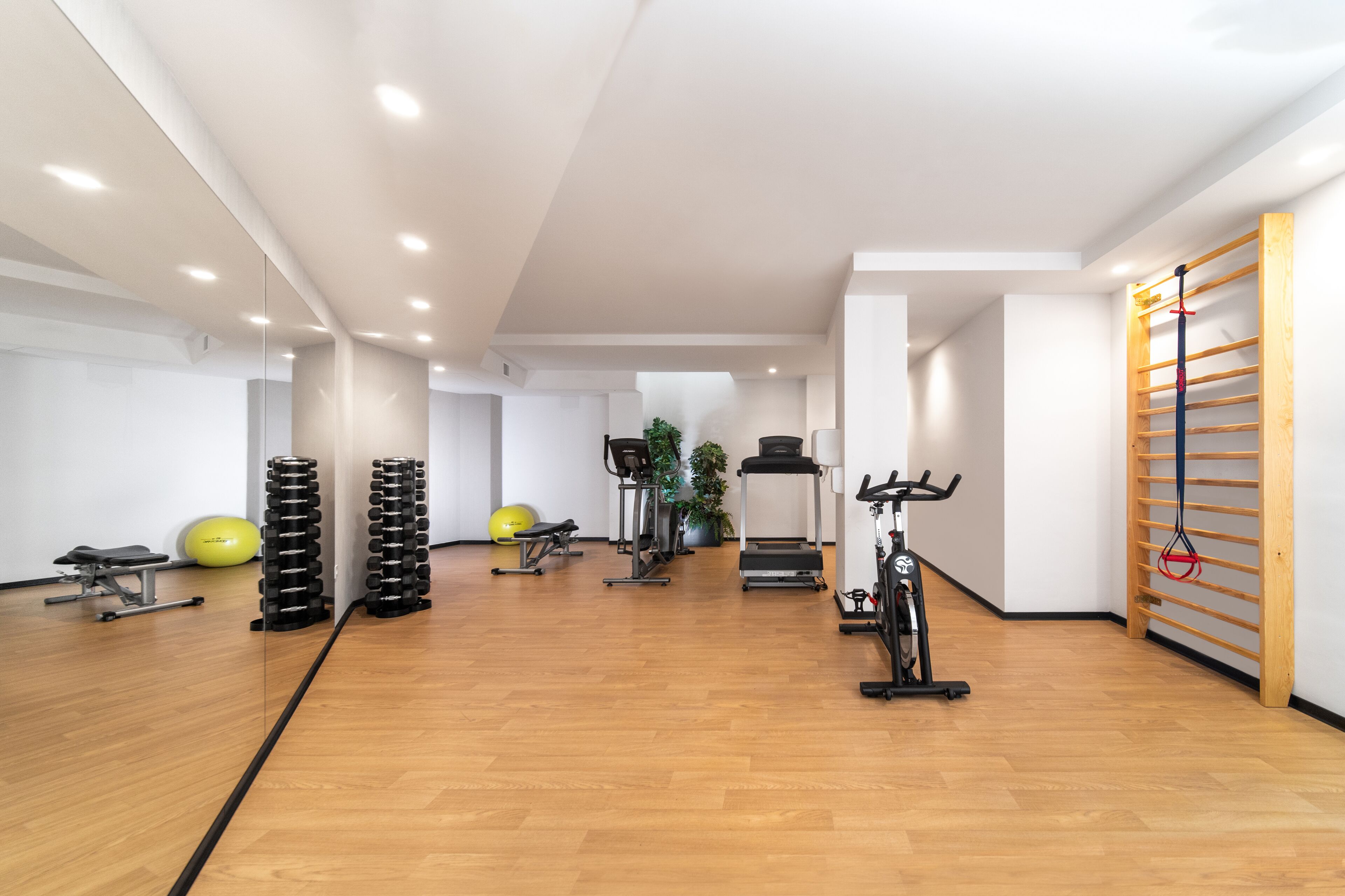 Un gimnasio amplio con suelo de madera, equipamiento de ejercicio y un espejo grande.