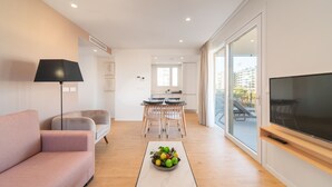 A modern living room with a sofa, a coffee table with fruit, a TV, and a dining area with chairs and a table. - Ahoy Apartments (El Campello)