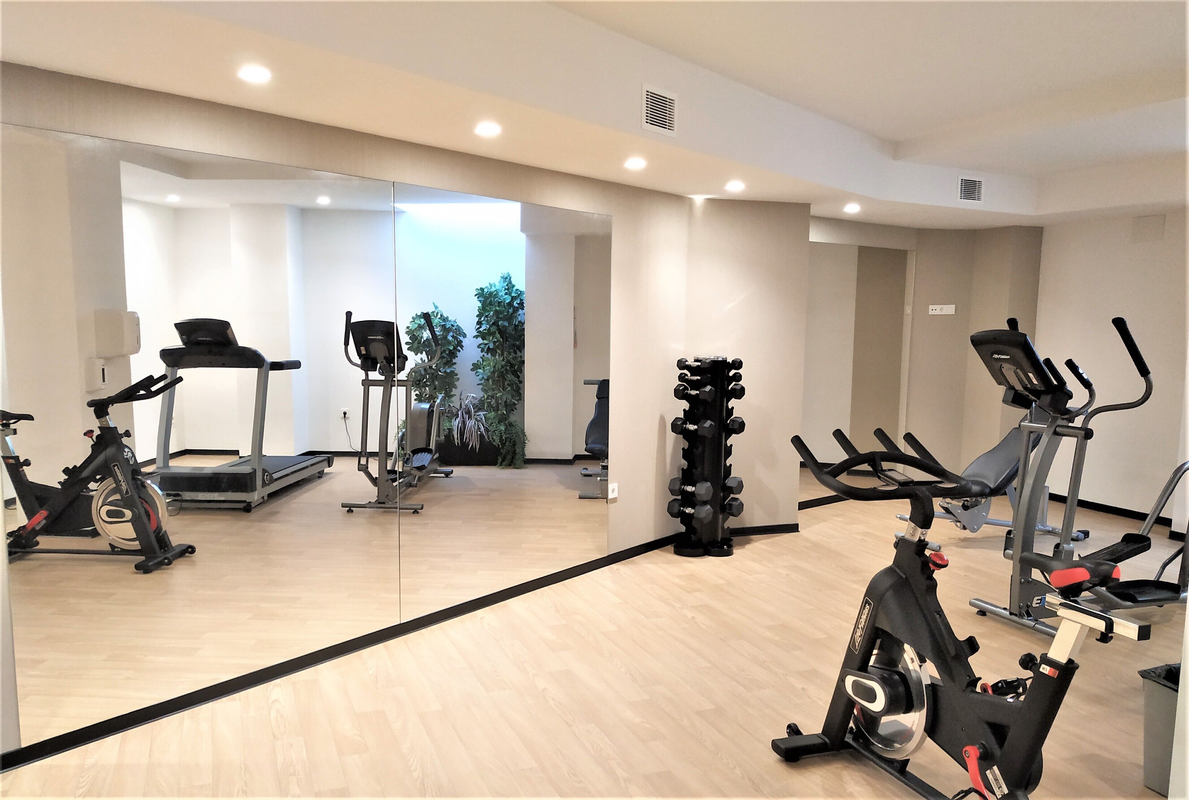 A gym with exercise equipment, a treadmill, and a mirror reflecting the space.